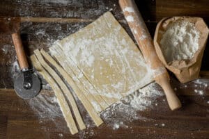 top view of a dough stripped pastry for cooking homemade pasta on a wooden table background, home cooking concept, close-up, flat lay