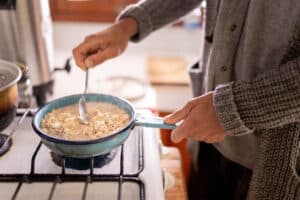 Young man is preparing soaked oats for breakfast using a gas stove. Concept of healthy diet