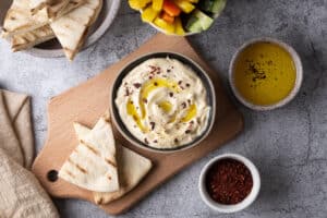 Hummus seasoned with olive oil with pita bread on a cutting board on a gray background, vegetable dip and a snack.