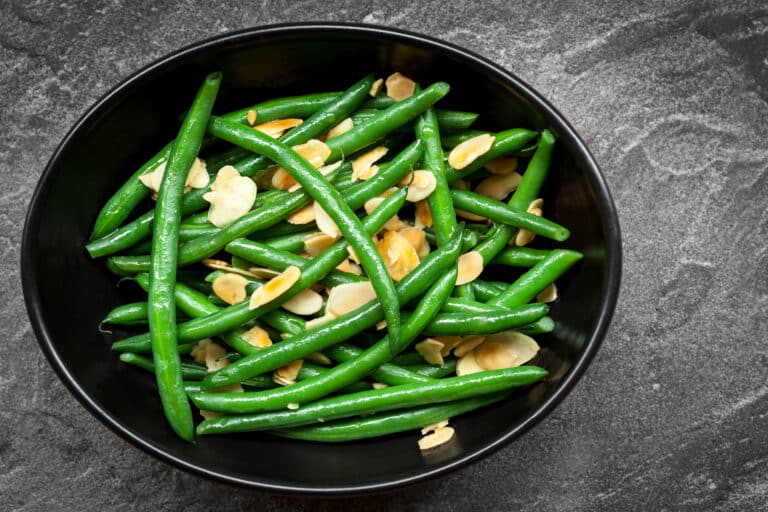 Green beans with toasted almonds, in black bowl over dark slate. Overhead view.
