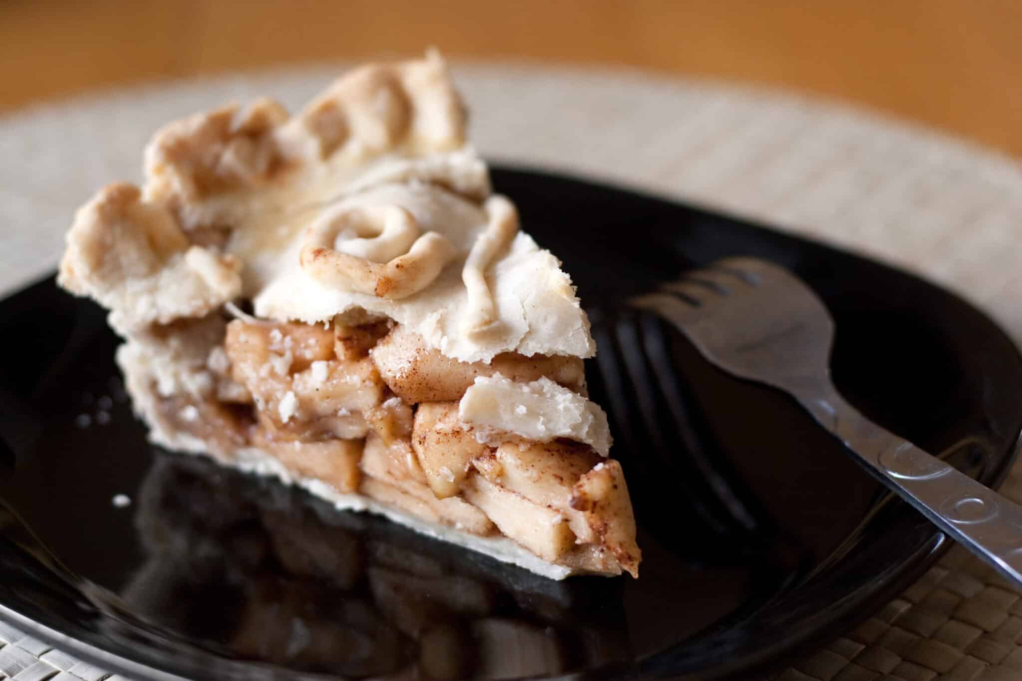 A piece of fresh homemade apple pie on a black plate. Shallow depth of field.