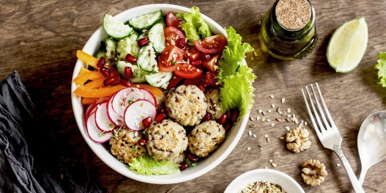 a white bowl with a colorful salad and turkey meatballs on a wood counter top