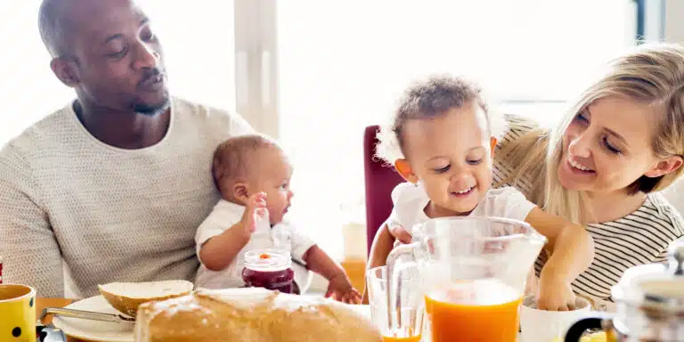 two smiling parents with two kids at the breakfast table with bread and juice