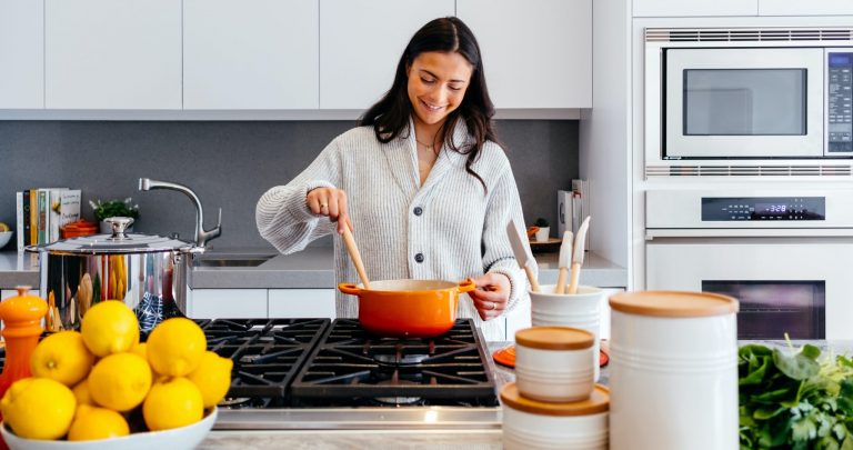 woman in a thick grey sweater cooking in an orange dutch oven over a gas stove