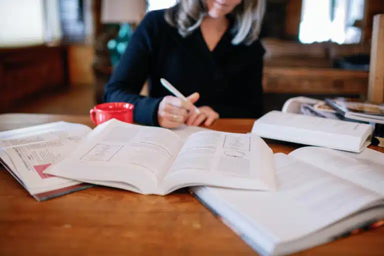 cropped image of woman meal planning with cluttered cookbooks and handwriting a shopping list