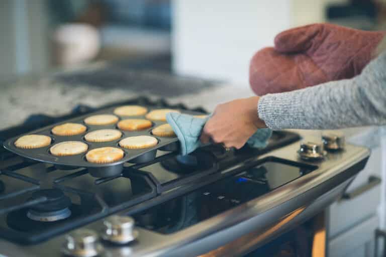 cropped image of woman taking muffins out of the oven with oven mits