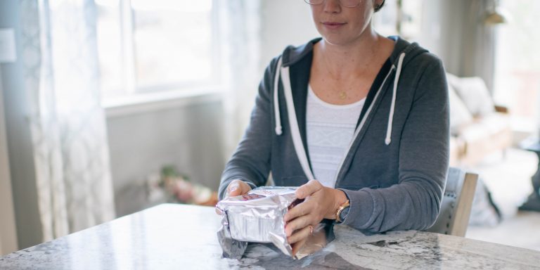 cropped image of a woman wrapping aluminium foil around a casserole for the freezer