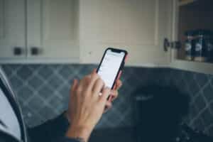 Cropped image of a hand holding a phone in a kitchen with a shopping list on screen