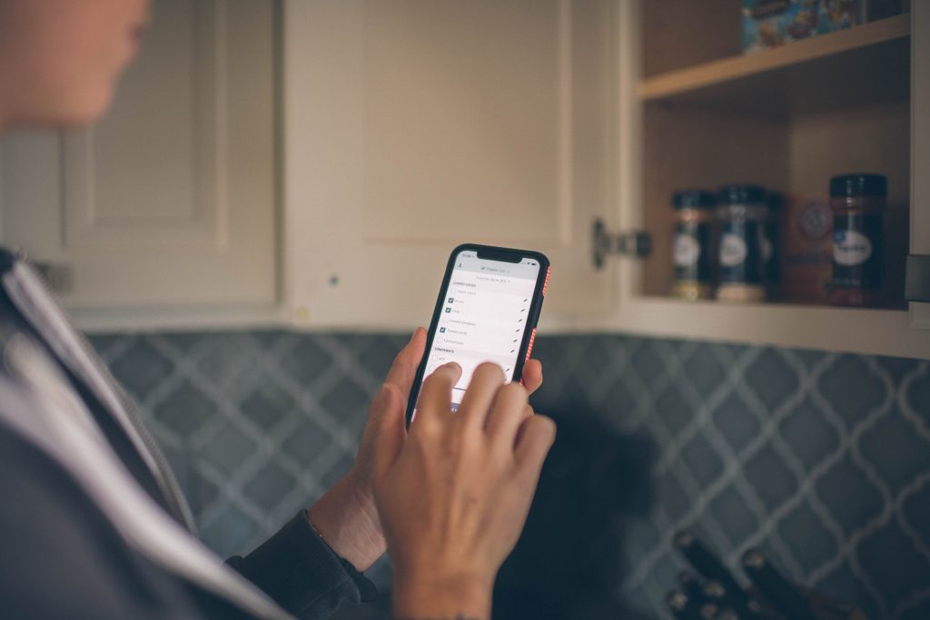 Cropped image of a person holding a phone in the kitchen with a shopping list loaded