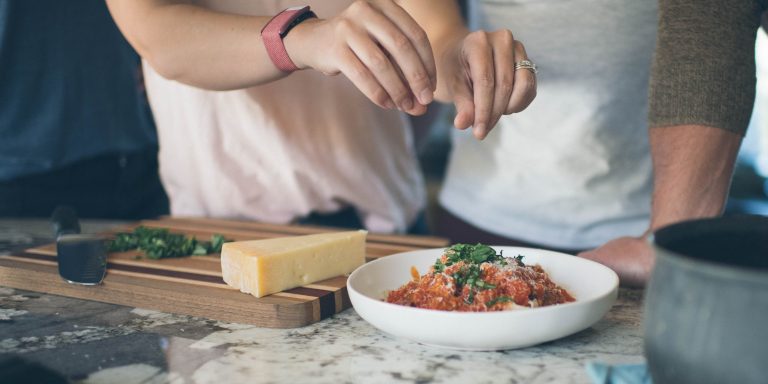 a cropped image of hands sprinkling chopped parsley onto a pasta dish with red sauce