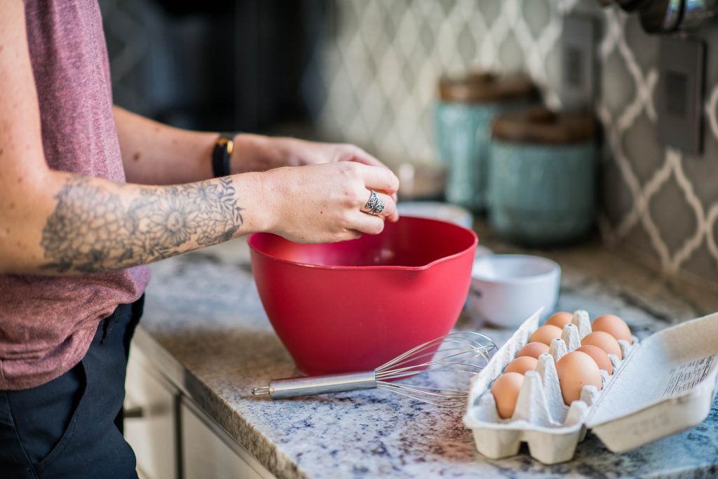 cropped image of a woman breaking an egg into a red mixing bowl