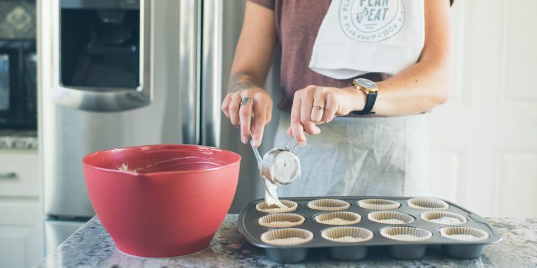 cropped image of a woman putting muffin batter into a muffin tin