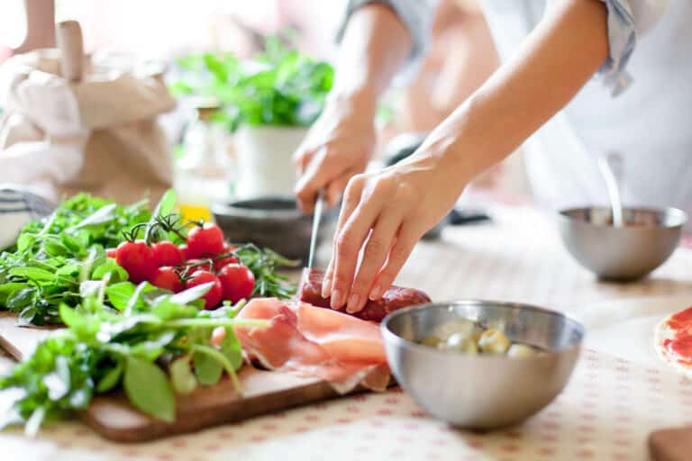 cropped image of woman's hands chopping vegetables and meat on a cutting board