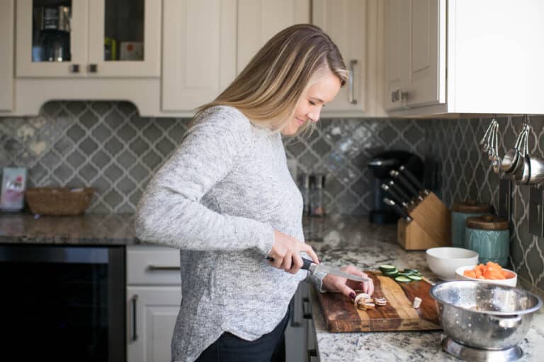 a young woman smiling as she cuts mushrooms in a kitchen