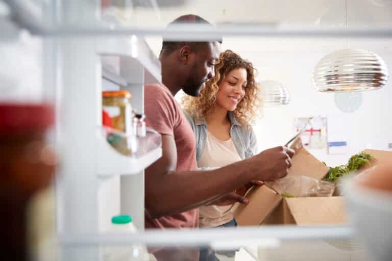 View Looking Out From Inside Of Refrigerator As Couple Unpack Online Home Food Delivery