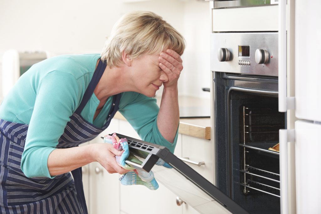 Woman Looking In Oven And Covering Eyes Over Disasterous Meal