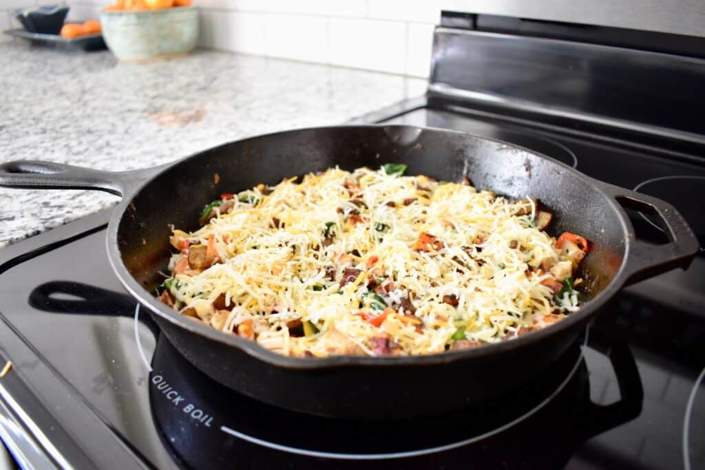 cooked meat and vegetables covered in shredded cheese in a cast iron pan