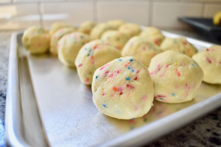 cookie dough with sprinkles rolled into balls on a flat cookie sheet.