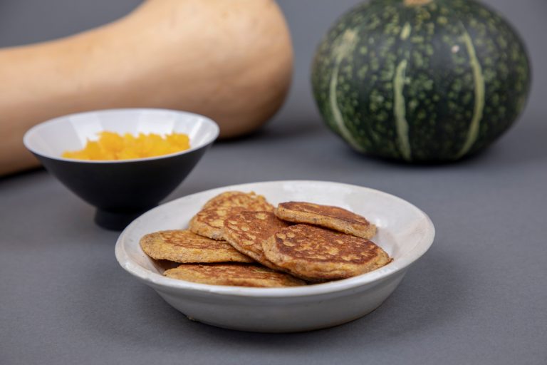 pancakes in a white bowl with squash in the background, on a grey backdrop