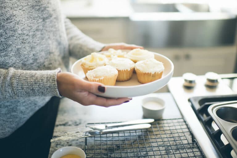 cropped image of a woman holding a plate of frosted vanilla cupcakes