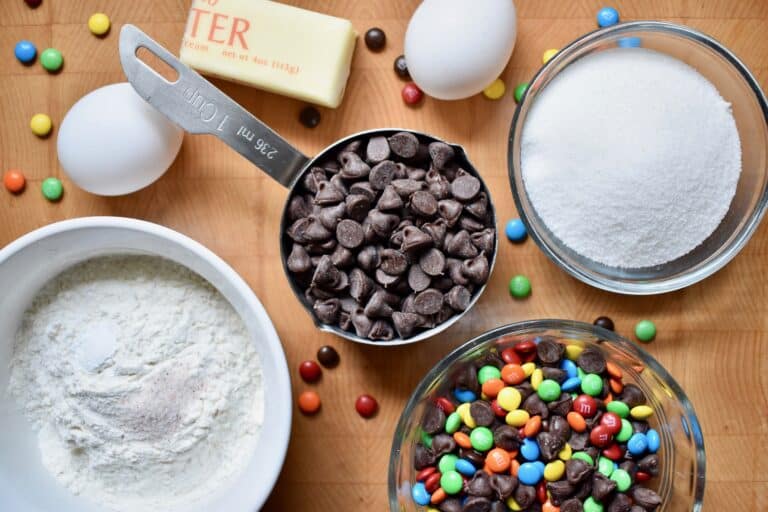 overhead shot of brownie ingredients, chocolate chips, sugar, flour, eggs and buttoner on a brown table