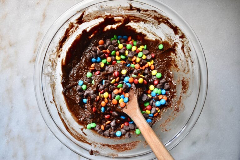 overhead shot of mini m&ms added to the brownie batter in a glass bowl