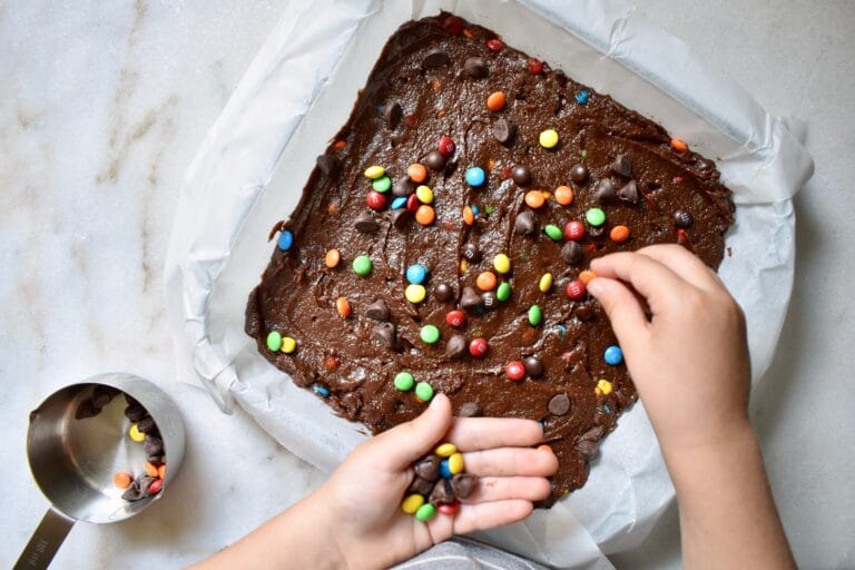 overhead shot of brownies in pan and a child's hands adding m&ms to the top