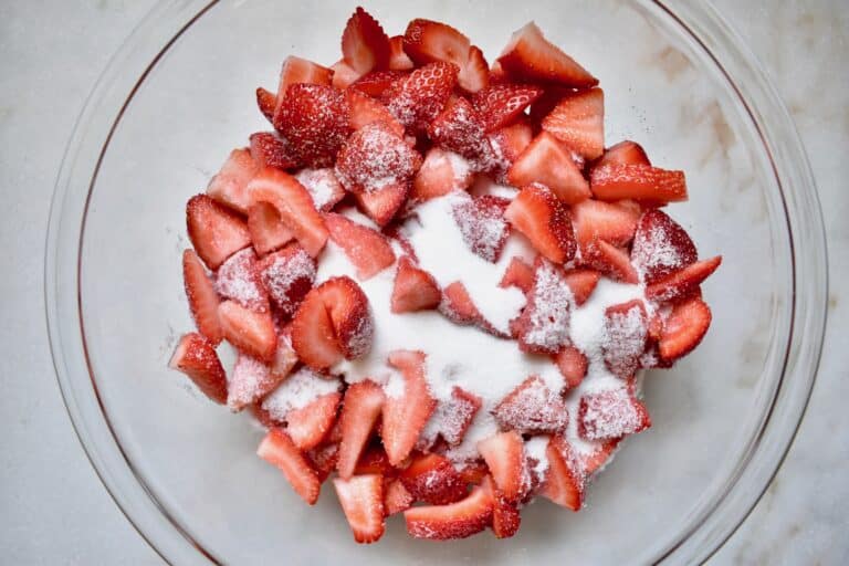 overhead shot of cut strawberries and sugar in a glass bowl