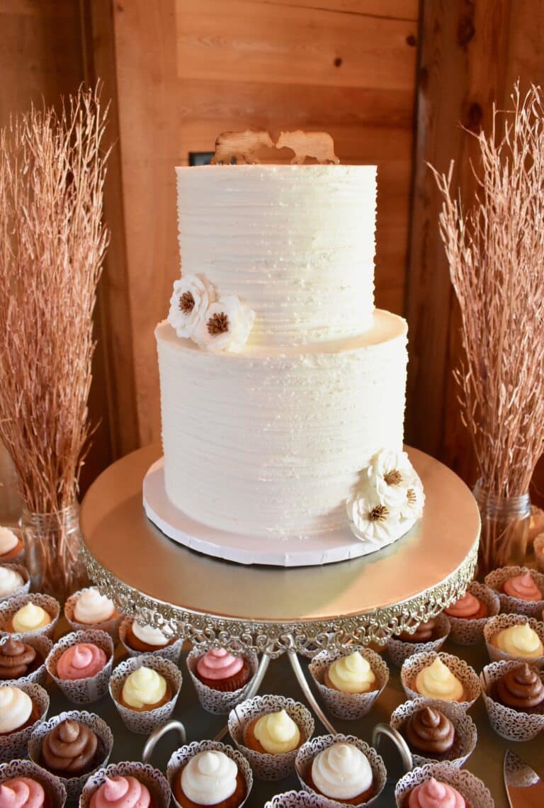 side image of two-tier white wedding cake with cupcakes at the bottom