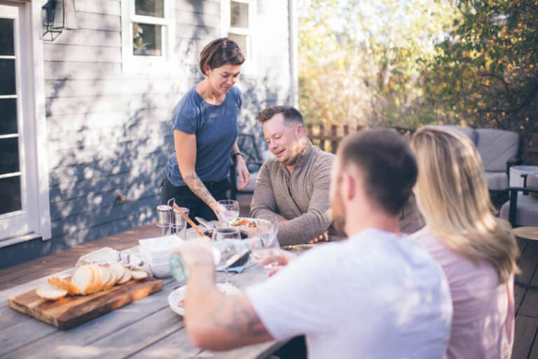 four friends around an outdoor dinner table, serving food and drinks