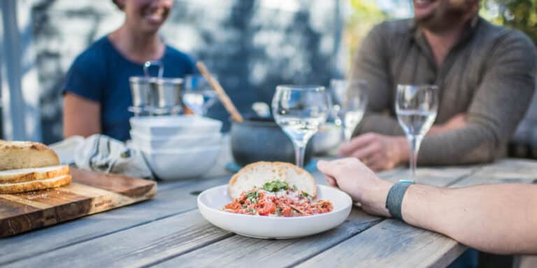 cropped image of dinner party with focus on plate of spaghetti and wine glasses