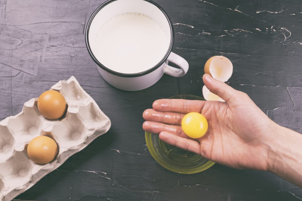 cropped image of a hand separating a yolk from an egg for eggnog