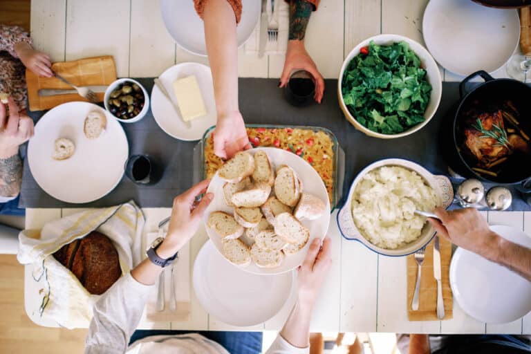 overhead image of a plate of bread being passed across a table full of food