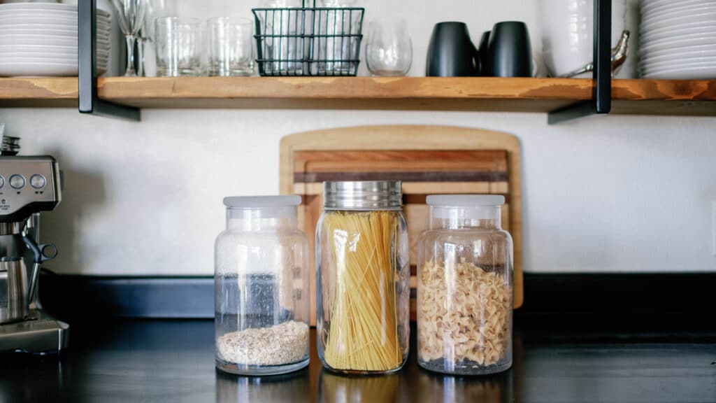 three glass jars on a black kitchen countertop filled with pasta