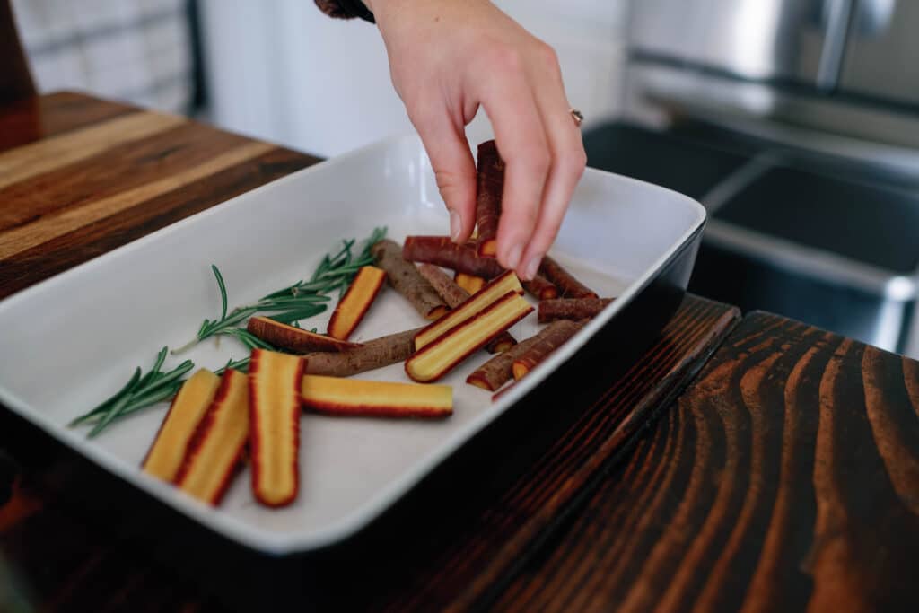 cropped image of a woman placing sliced colorful carrots into a baking dish