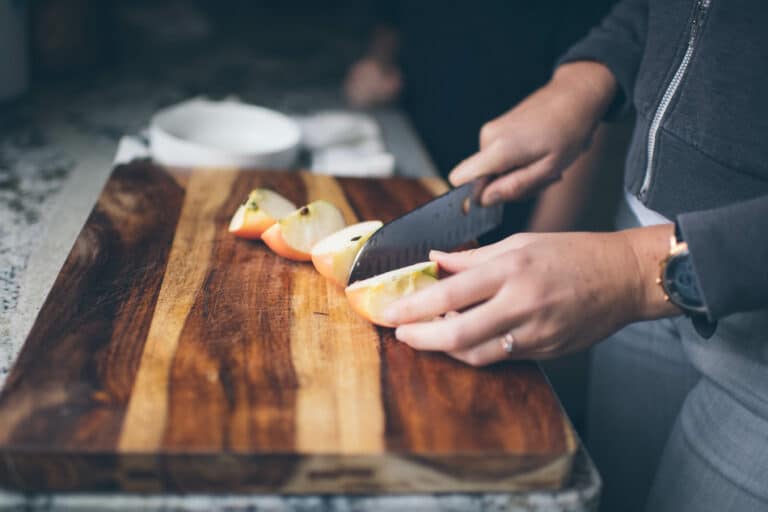 cropped image of a woman cutting an apple into wedges on a wooden cutting board