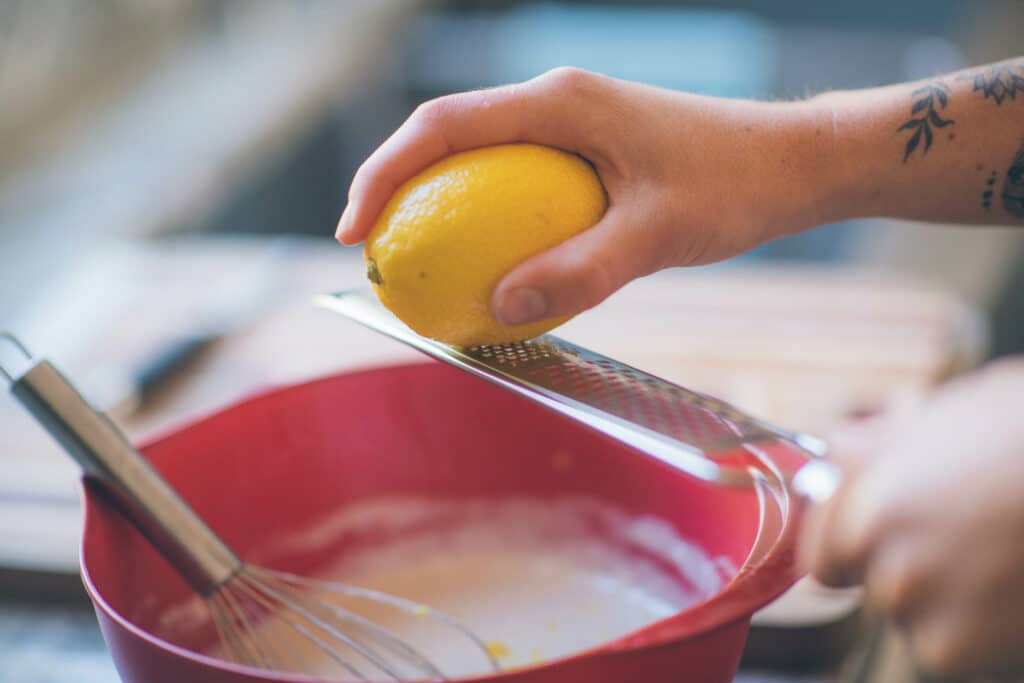 cropped image of a lemon being zested into a red bowl