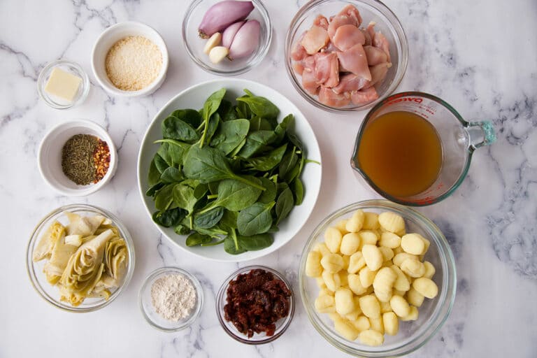Overhead image of raw ingredients for the tuscan chicken gnocchi recipe laid out on a marble counter top
