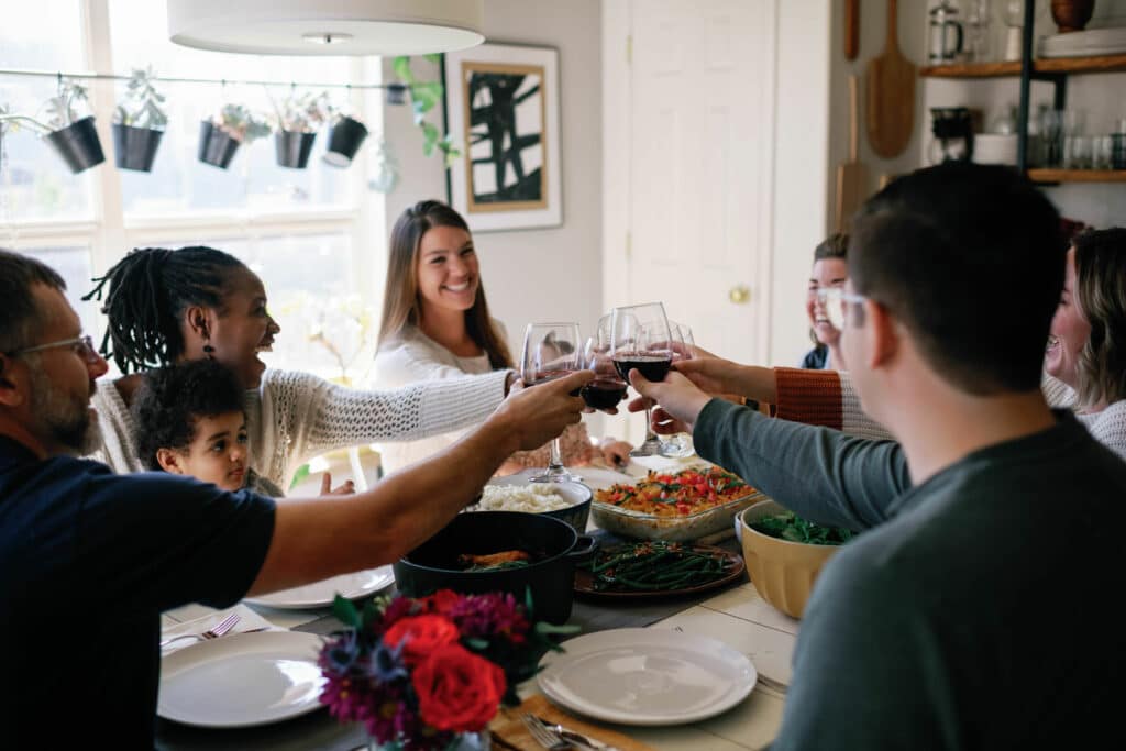 friends gathered around a table full of food, cheersing their wine glasses and smiling