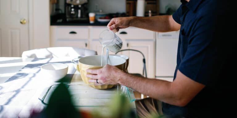 cropped image of a man pouring milk from a measuring cup into a big yellow bowl