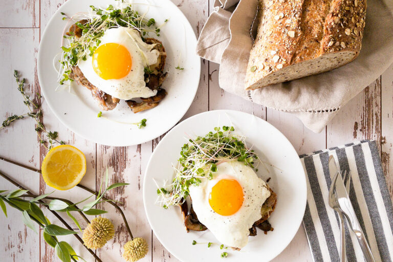 overhead view of two open faced breakfast sandwiches with bright sunny side up eggs on top on white plates