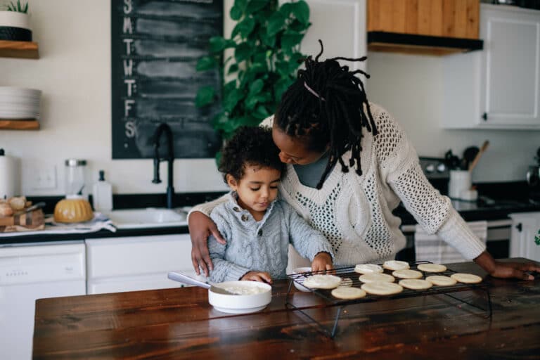 mother kissing her son's forehead as they decorate sugar cookies in the kitchen