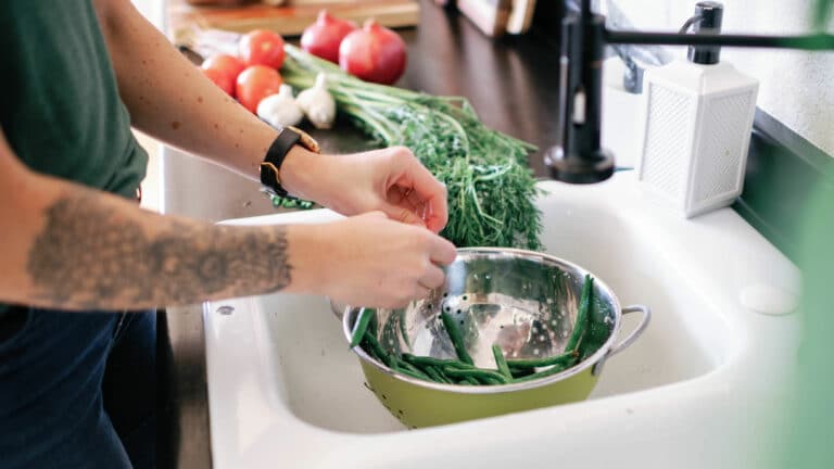 cropped image of a person washing green beans in a colander