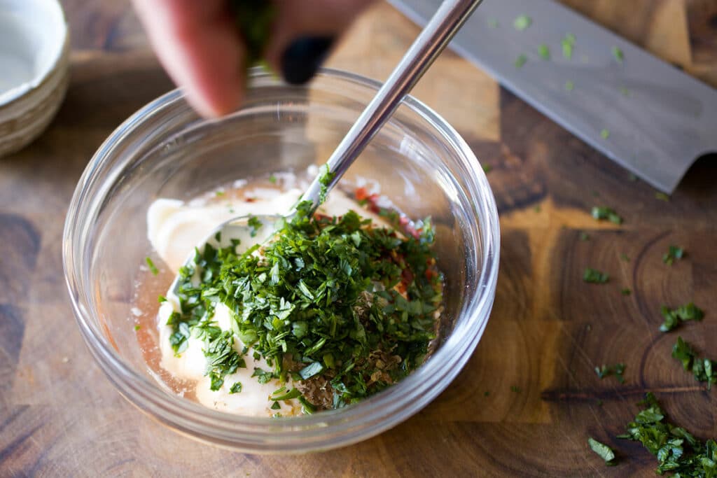 chimichurri ingredients being mixed in a small glass bowl on a wooden background