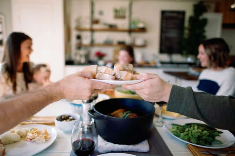 image of a plate of bread being passed from one person to the other with a table of people in the background