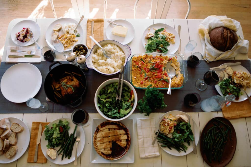 overhead shot of dinner table full of dishes and prepared food with evening light streaming in through windows