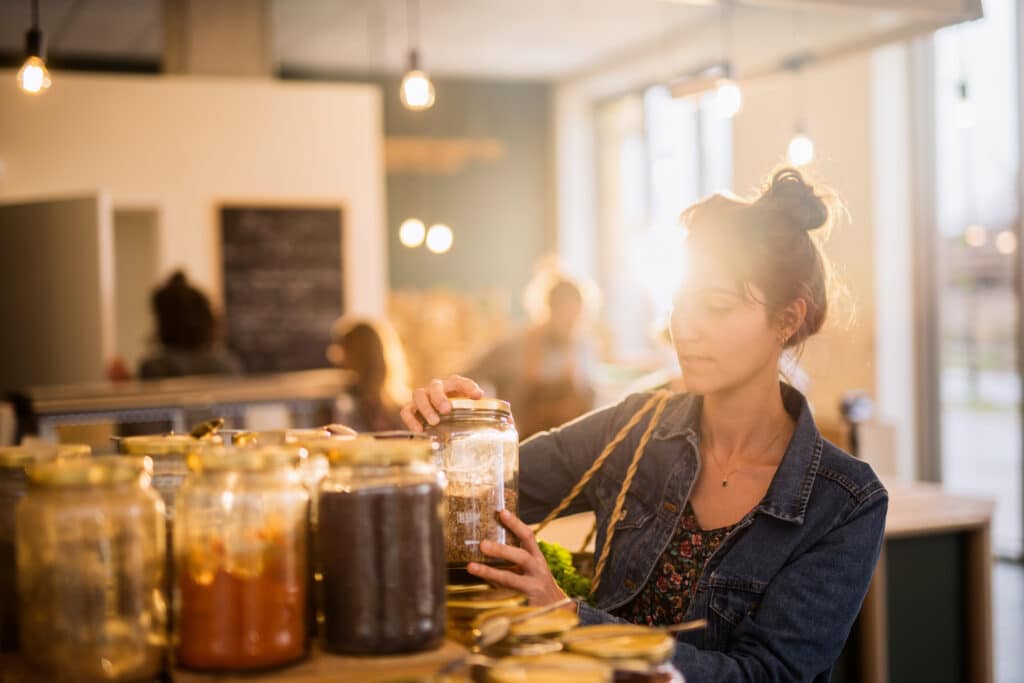 Beautiful young woman shopping in a bulk food store. She buys organic spices in jars. Focus on Jar