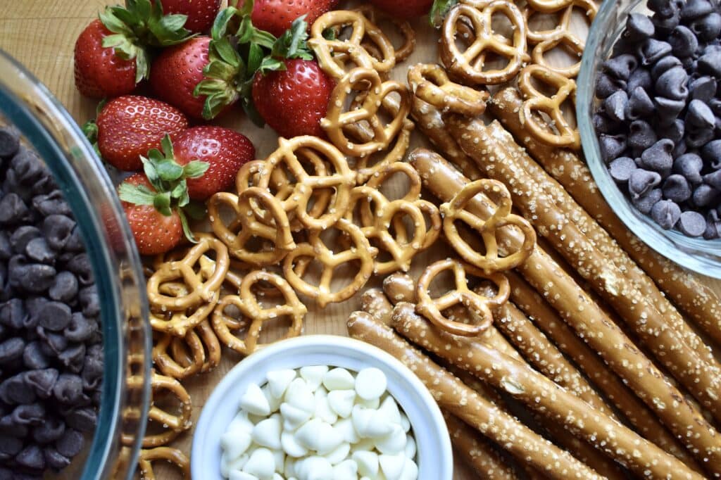 close up of ingredients for dessert charcuterie board including chocolate, pretzels, and strawberries
