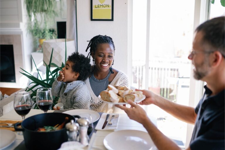 woman holding a small child passing a plate of bread to a man at the dinner table