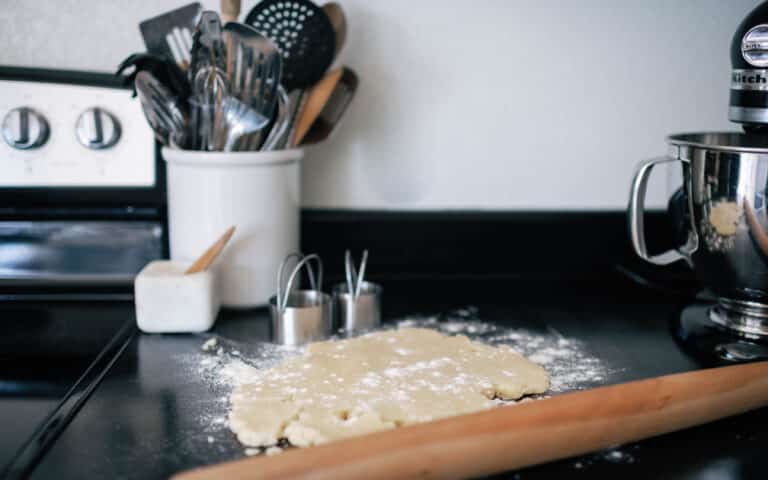 cookie dough rolled out on a black countertop with flour sprinkled around and kitchen utensils in the background